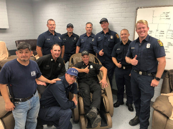 Group of firefighters posing for a photo in a room with a massage chair.