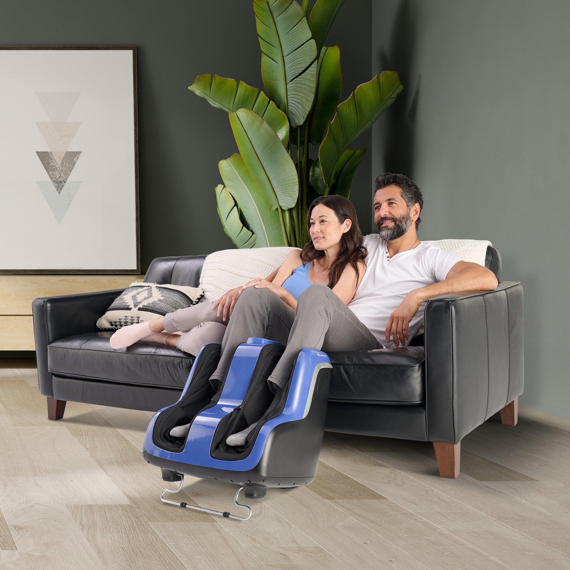 Reflex SOL Plus foot and calf massager shown in modern living room with couple relaxing on leather couch