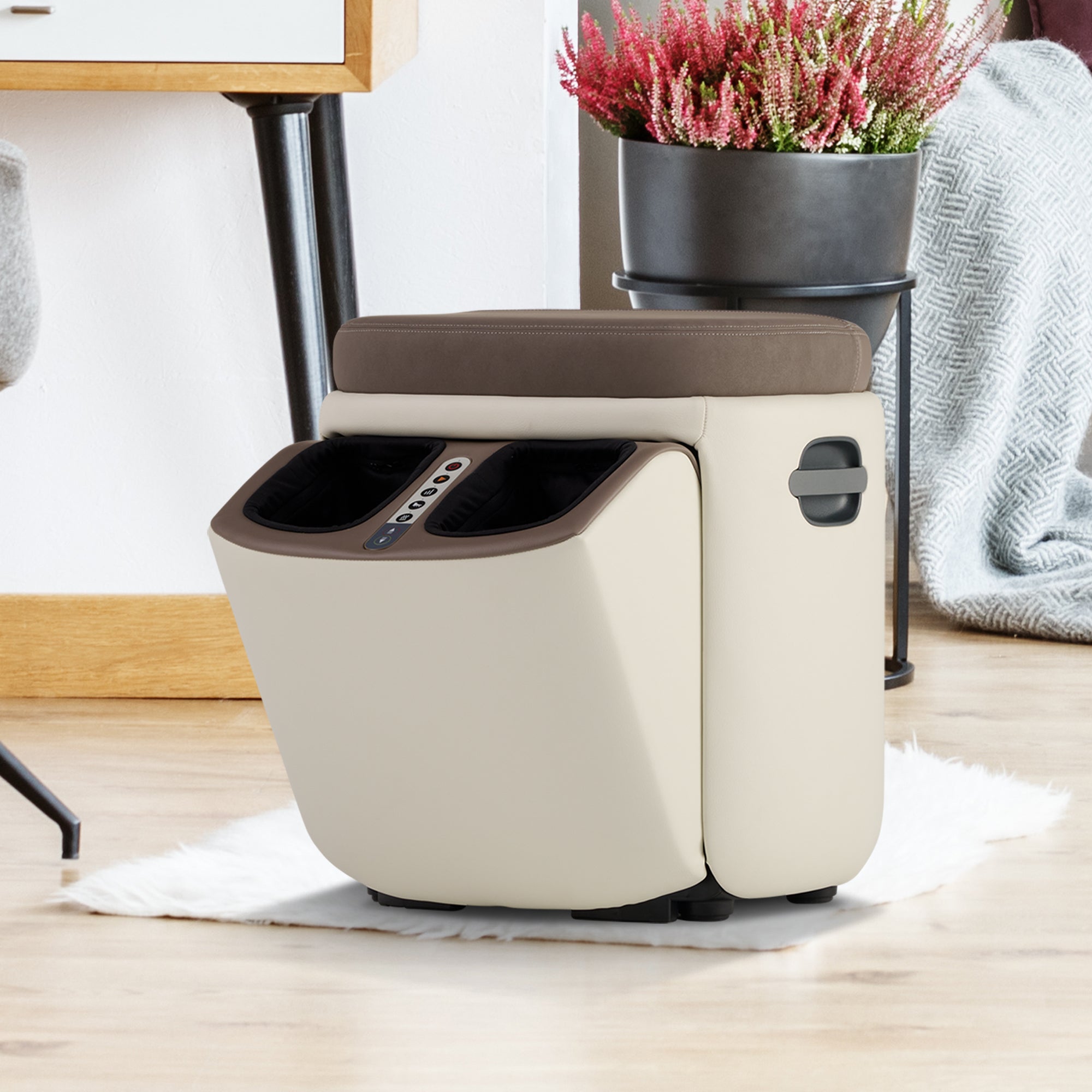 Reveal Ottoman Massager in cream and brown shown as footrest with built-in massage ports beside potted pink flowers