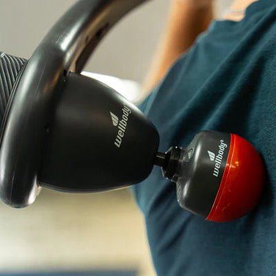 Person holding a black and red massage gun with 'Wellbody' branding.